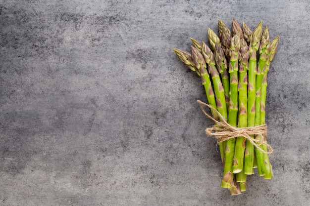 Banches of fresh green asparagus,  and vegetables on concrete surface, top view