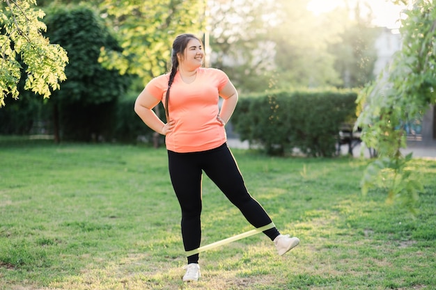 Band exercise Weight control Active lifestyle Body positive Happy motivated overweight obese woman in sportswear fitness training in sunny green spring park landscape