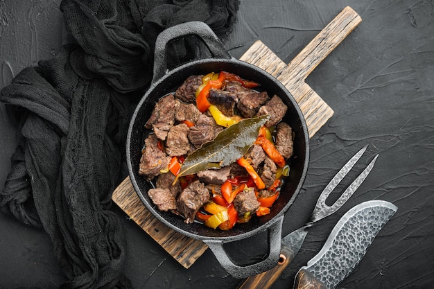 Bangin beef stew served, in cast iron frying pan, on black stone background, top view flat lay, with copy space for text