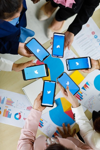 Bangkok/Thailand - August 06, 2021: People hold smartphones in different brands and various operating systems with logos of Twitter social applications.