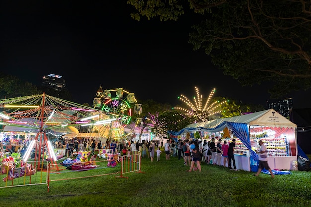 Bangkok Thailand Dec 8 2022 Crowds of people walk into a beautifully lit amusement park during the Red Cross Fair to be held from December 818 2022 The image is blurred by the movement