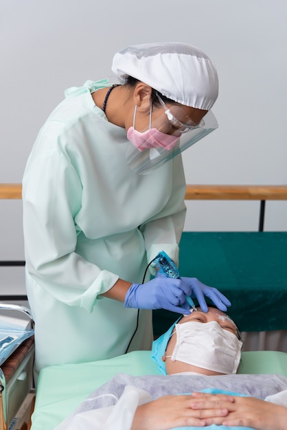 Bangkok, Thailand - May 30, 2020 : Unidentified Asian woman eyebrow tattooing by specialist in Eyebrow tattoo or embroidery clinic use COVID-19 prevention policy protect by use mask and face shield