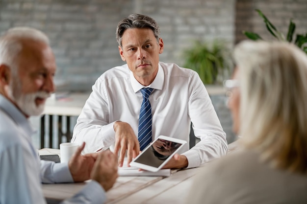 Bank manager using touchpad while communicating with senior couple during a meeting in the office