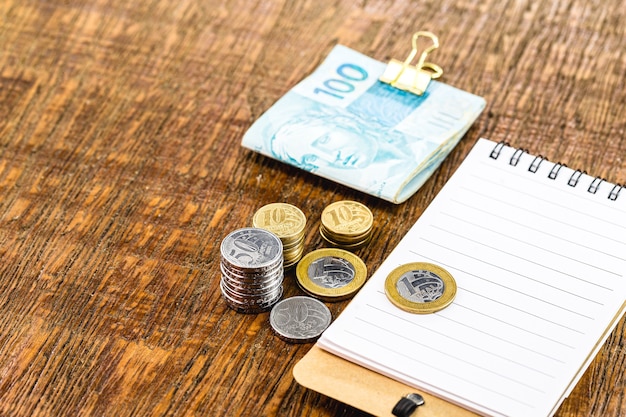 Banknotes and coins of brazil money, on table with notepad and pen