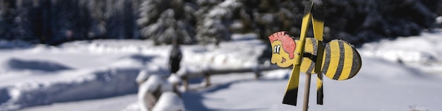 Banner 41 with a weather vane in the form of a cheerful bee against the background of mountains and a dense spruce forest in bokeh