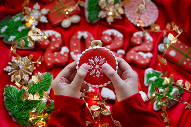 Banner for Christmas and New Year gingerbread cookies in children hands and numbers 2022 snowflakes Christmas trees toys garlands on red silk fabric background