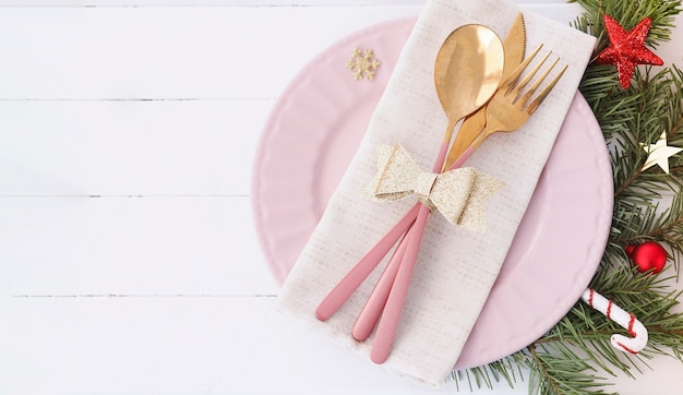 Banner of Christmas table setting. pink plate, cutlery with gold bow, fir branches and stars. copy space.