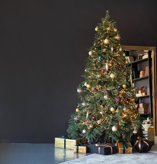 Banner Christmas tree with golden decorations and lights near black wall and vintage miracle in dark interior with copy space place for text