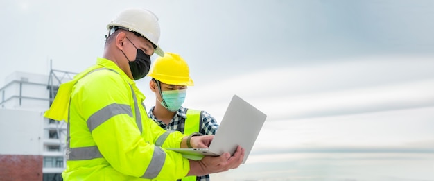 Banner : Civil engineer wearing mask inspect construction site structure and plans in laptop. Civil engineer inspects the actual construction site. Civil engineer hold laptop to inspect the building.