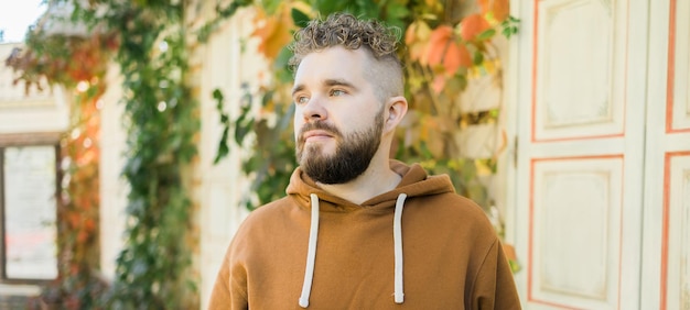 Banner Close up shot of curly European male with beard wears switshot outdoors copy space Handsome man with crisp light hair