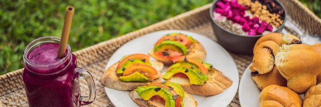 Banner long format breakfast on a tray with fruit buns avocado sandwiches smoothie bowl standing on