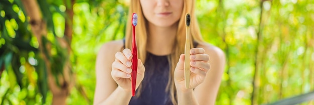 BANNER LONG FORMAT Woman holds eco natural bamboo toothbrush and in other hand plastic toothbrush rustic background sustainable lifestyle concept zero waste choice plastic free items