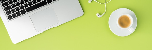 Banner of metallic laptop keyboard white earphones and coffee cup on light green background