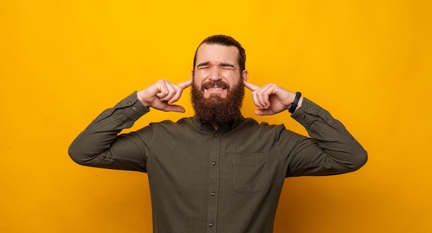 Banner photo of a man covering ears with fingers in order not to hear Studio panorama photo over yellow background