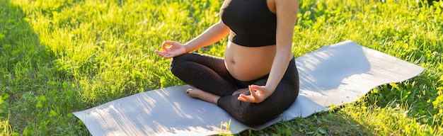 Banner pregnant woman is meditating while sitting on yoga mat on lawn sunny summer evening copy space Concept of pacification and energy boost