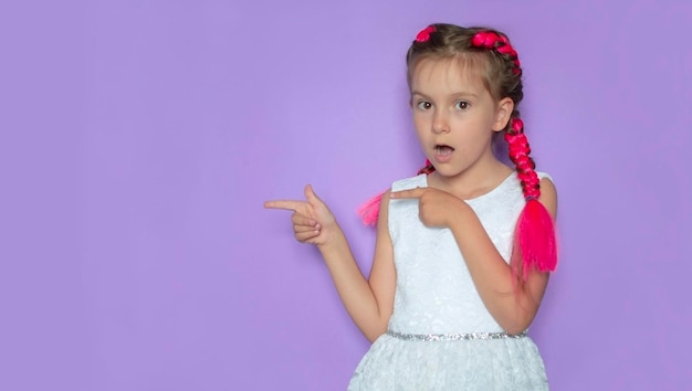 Banner A smiling charming girl with pink hair on a purple background pointing her finger to the side at different places to copy selects one of them by pointing her finger A place for advertising