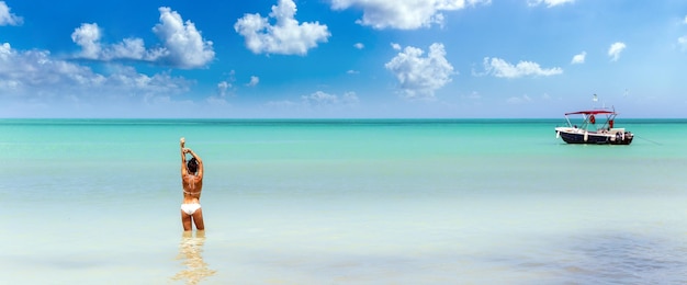 Banner of a woman standing in warm turquoise clean sea in tropical paradise enjoying holidays with a boat on the side