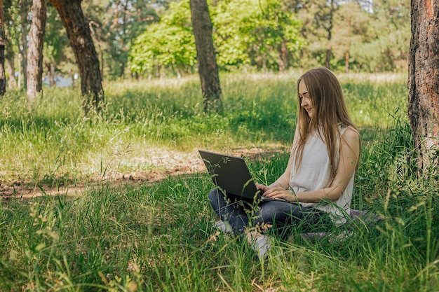 On the banner a young girl works with a laptop in the fresh air in the park sitting on the lawn The concept of remote work Work as a freelancer The girl takes courses on a laptop and smiles