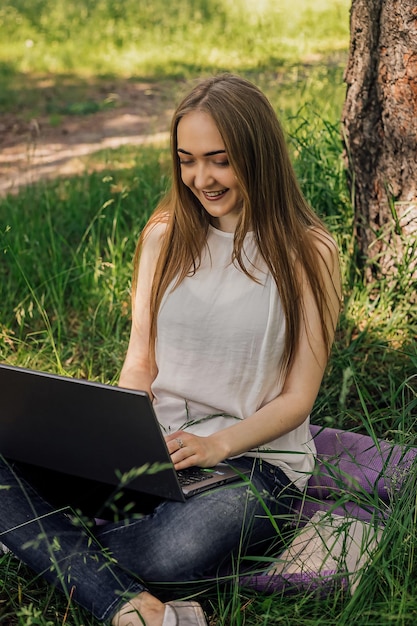 On the banner a young girl works with a laptop in the fresh air in the park sitting on the lawn The concept of remote work Work as a freelancer The girl takes courses on a laptop and smiles