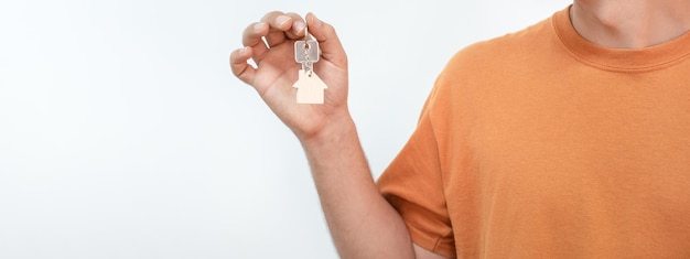 Banner of young man with the new home keys. Keychain in the shape of a wooden house on white backgro