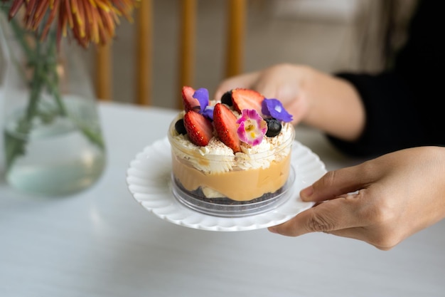 A Banoffee Pie is served in a plastic cup, adorned with flowers and strawberries as decoration.