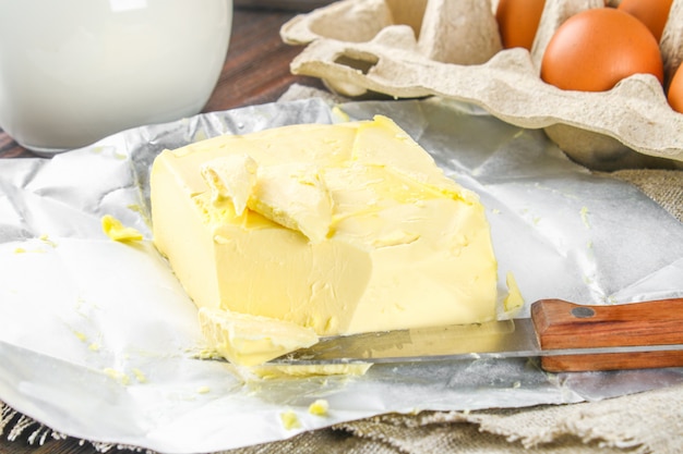 A bar of butter is cut into pieces on a wooden board with a knife