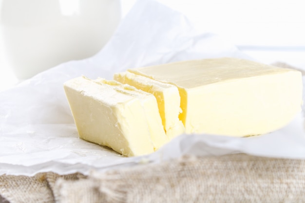 A bar of butter on a wooden board with a knife, on a white table. Ingredients for cooking.