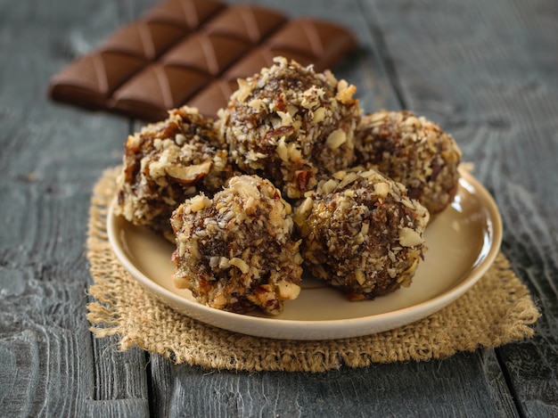 A bar of chocolate and balls of nuts, dried fruits and chocolate on a black table. Delicious fresh home-made candies.