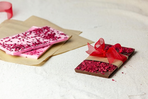 A bar of chocolate with pieces of berries tied with a red bow pink chocolate lies nearby Gift idea