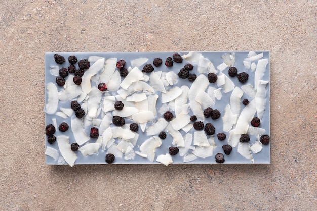 A bar of white chocolate stained with tea Anchan with coconut slices and freeze-dried blueberries on a light background. Top view, flat lay.