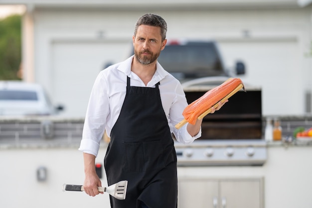 Barbecue master in chef apron hold salmon fillet on bbq millennial man in apron for barbecue