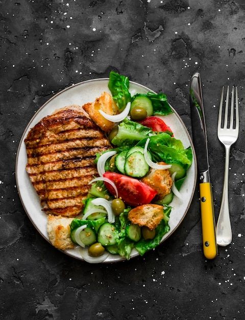 Barbecue pork chop and Italian panzanella salad on a dark background top view Mediterranean cuisine concept