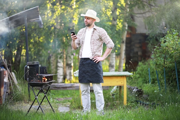 Barbecue time. European man in hat waiting for grilled food. He is sitting near fire and rest.