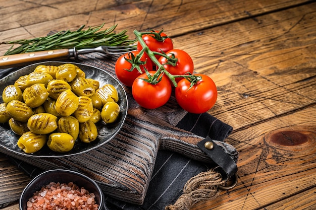 Barbecued organic olives with herbs in plate Wooden background Top view Copy space