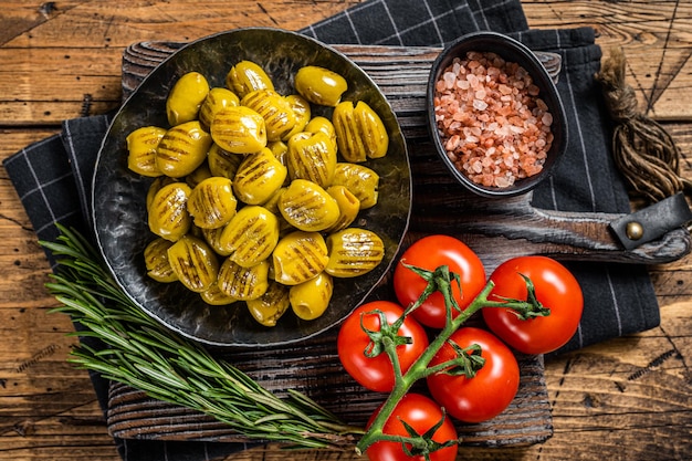 Barbecued organic olives with herbs in plate. Wooden background. Top view.