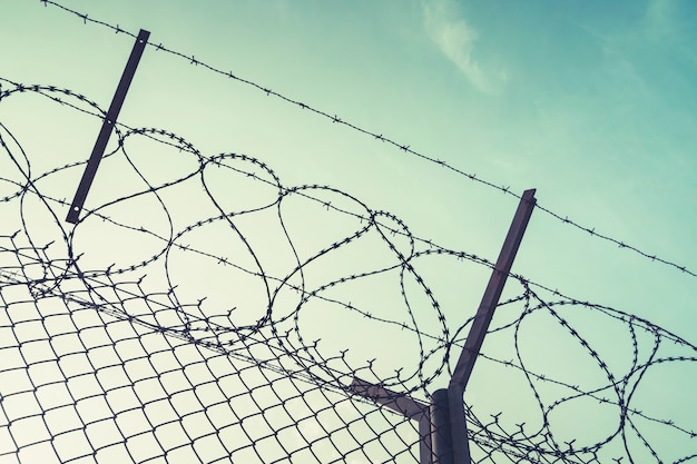 Barbed wire steel wall against immigations. Wall with barbed wire on the border of 2 countries. Private or closed military zone against the background blue sky.