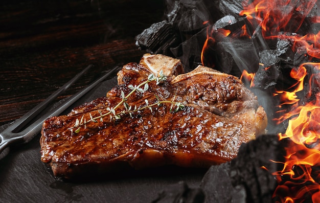 Barbeque steak on a black slate board with meat fork and grill coals