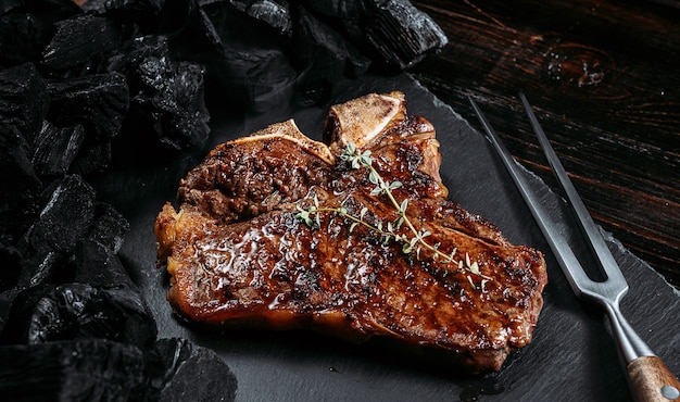 Barbeque steak on a black slate board with meat fork and grill coals