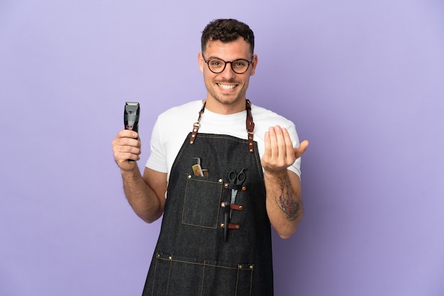 Barber caucasian man in an apron isolated on purple inviting to come with hand