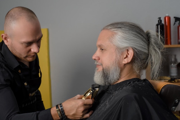 Barber cutting and styling the beard of a grayhaired man Barber shop for men