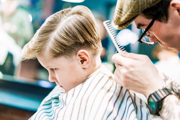 A barber holds a comb doing haircut for a boy