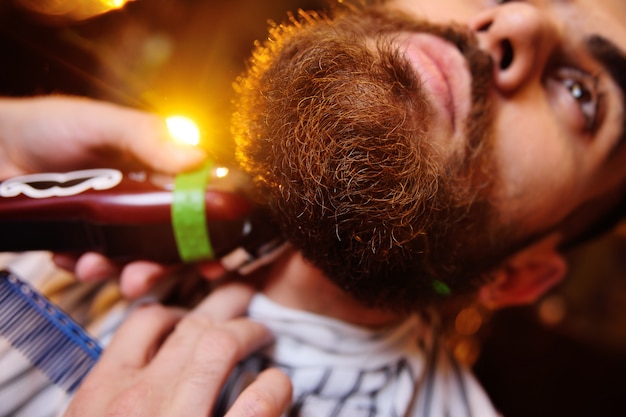 Barber is shaping his beard to the client in barbershop