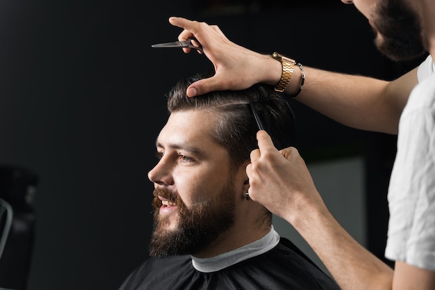 Barber making hairstyle for confident bearded hipster. Advertising for barbershop and men's beauty salon.