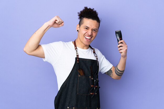 Barber man in an apron over isolated purple wall celebrating a victory