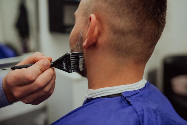 The barber paints the beard and the mustache of the young man in the barbershopSelective focus High quality photo