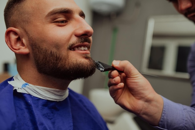 The barber paints the beard and the mustache of the young man in the barbershopSelective focus High quality photo