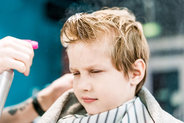 A barber's hand is splashing the water on boy's head