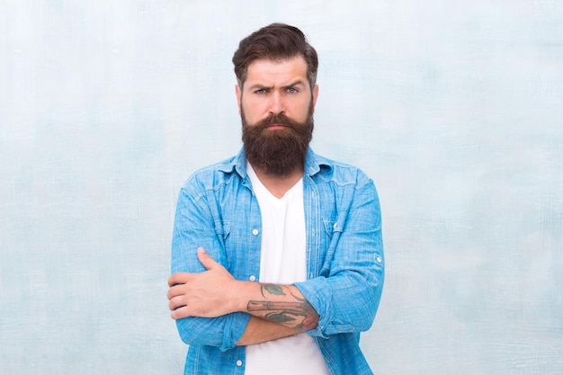 Barber salon Male beauty concept Well groomed macho Brutal handsome hipster man on grey wall background Bearded man trendy hipster style Hipster with beard and mustache wear denim shirt