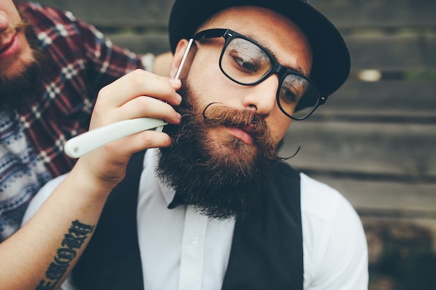 Barber shaves a bearded man in vintage atmosphere