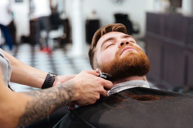 Barber shaving beard of his client with hair clipper